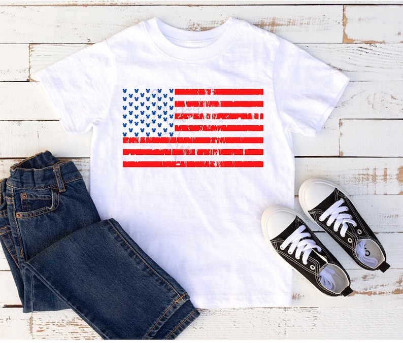 May include: White t-shirt featuring a distressed American flag design with blue Mickey Mouse heads. The flag is red, white and blue.