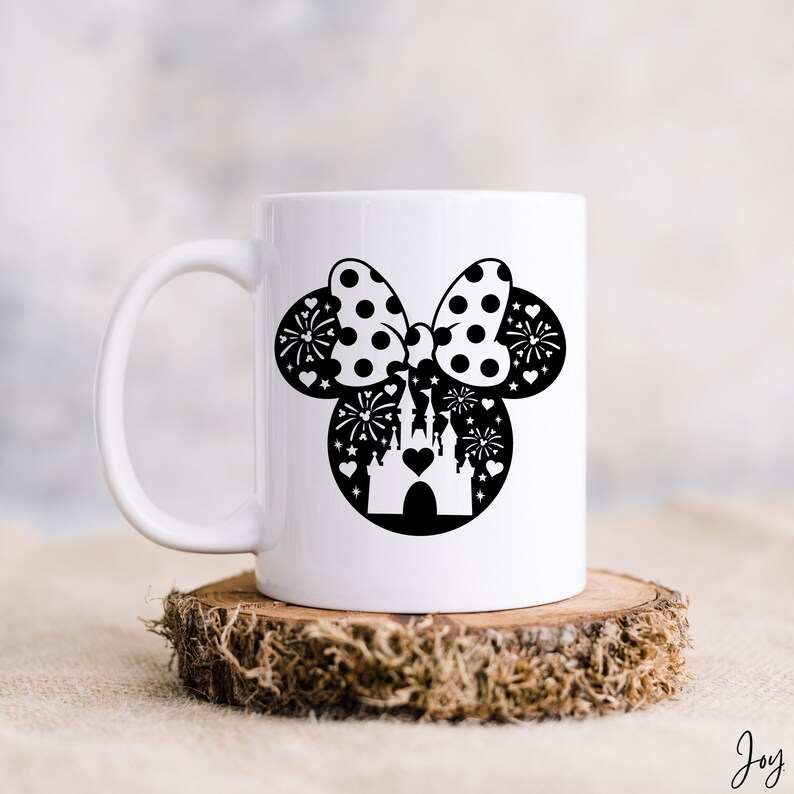 May include: White ceramic mug with a black silhouette of Mickey Mouse ears with a bow and a castle inside the ears. The bow is polka dotted and there are fireworks around the castle.