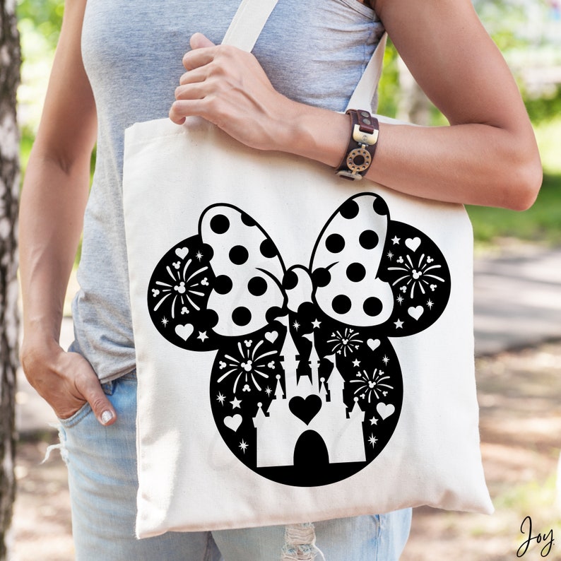 May include: A white tote bag with a black and white silhouette of Minnie Mouse's head with a bow and a castle inside. The bow has black polka dots and the castle has fireworks around it.