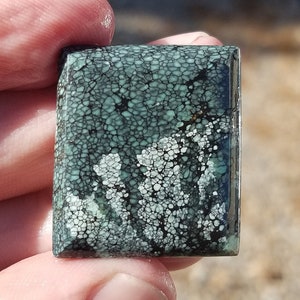 May include: A square, green and white, cabochon gemstone with a unique, mottled pattern. The stone is cut and polished, and has a smooth, glossy finish.
