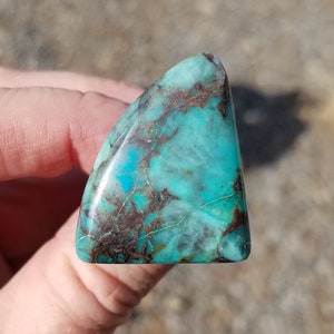 Puede incluir: Un cabujón de turquesa triangular con matriz marrón y un tono azul claro.