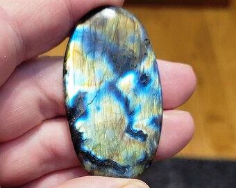 May include: A smooth, oval-shaped labradorite gemstone with iridescent blue, green, and gold colors.