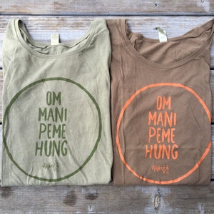 May include: Two t-shirts with a circular design featuring the text "OM MANI PEME HUNG" in green and orange lettering on a light green and brown shirt, respectively. The text is surrounded by a circle in the same color as the lettering.