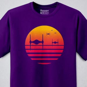 May include: Purple t-shirt with a retro sunset graphic featuring TIE fighters from Star Wars.