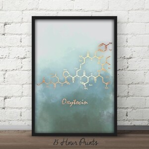 May include: A framed print with a watercolor background in shades of blue and green. The print features a gold chemical structure of the hormone oxytocin, with the word "Oxytocin" written in gold below the structure.