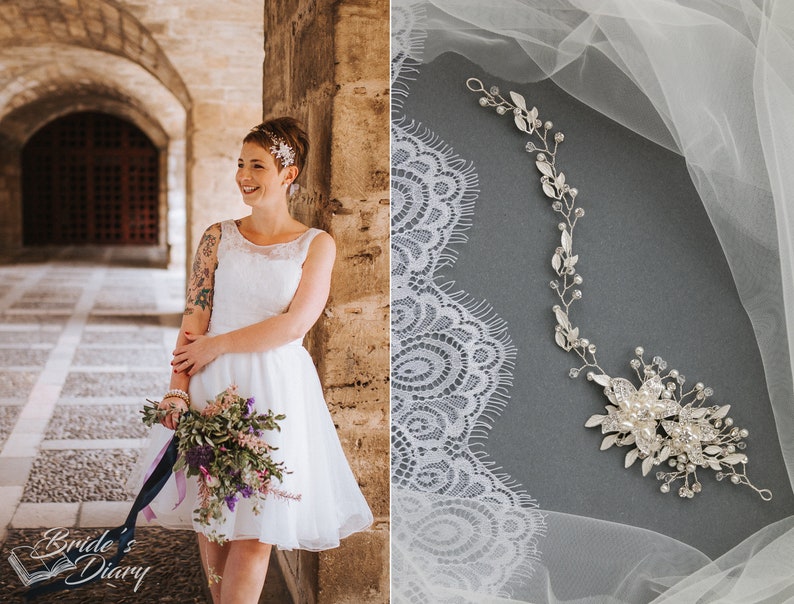May include: A bride wearing a white lace dress with a floral bouquet and a silver hairpiece. The bride is standing in a stone archway. The image also shows a silver hairpiece with rhinestones and leaves on a white lace fabric.