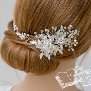 May include: A silver and pearl bridal hair comb with a floral design. The comb is worn in a woman's hair, which is styled in a bun.