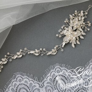 May include: Silver bridal hair vine with delicate leaves, pearl accents, and crystal embellishments. The vine is designed to be worn in the hair, and it is perfect for adding a touch of sparkle to any bridal look.