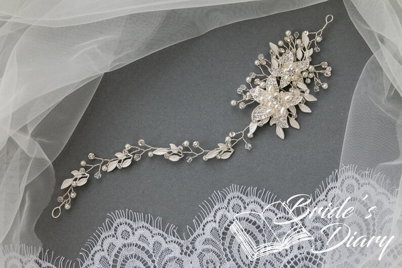 May include: Silver bridal hair vine with delicate leaves, pearl accents, and crystal embellishments. The vine is designed to be worn in the hair, and it is perfect for adding a touch of sparkle to any bridal look.