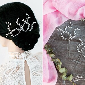 May include: Three silver hair pins with white pearl accents in the shape of branches. The hair pins are on a wooden surface with a pink fabric in the background. The text "Bride's Diary" is visible in the bottom right corner of the image.