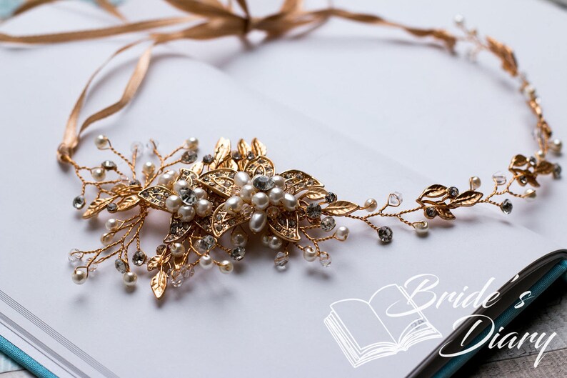 May include: Gold bridal hair vine with delicate leaves and pearl accents. The vine is adorned with a large floral design featuring gold and clear rhinestones.