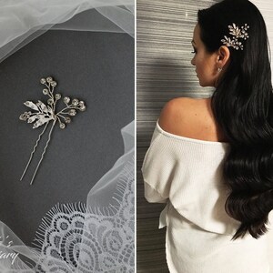 May include: A silver hair comb with crystal embellishments in the shape of a floral sprig. The comb is shown on a gray background with a white lace overlay. The comb is also shown in a model's hair.