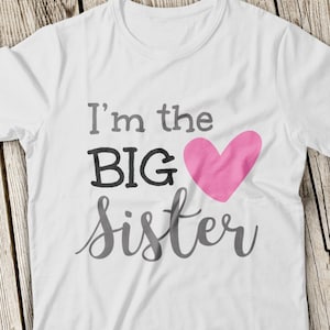 May include: White t-shirt with the text "I'm the BIG sister" in black and gray lettering. A pink heart is next to the word "BIG".