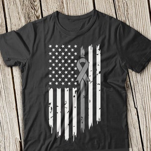 May include: Black t-shirt featuring a distressed American flag design with a gray ribbon. The flag has white stars and stripes, with the ribbon placed vertically through the center. The design has a vintage, worn look.