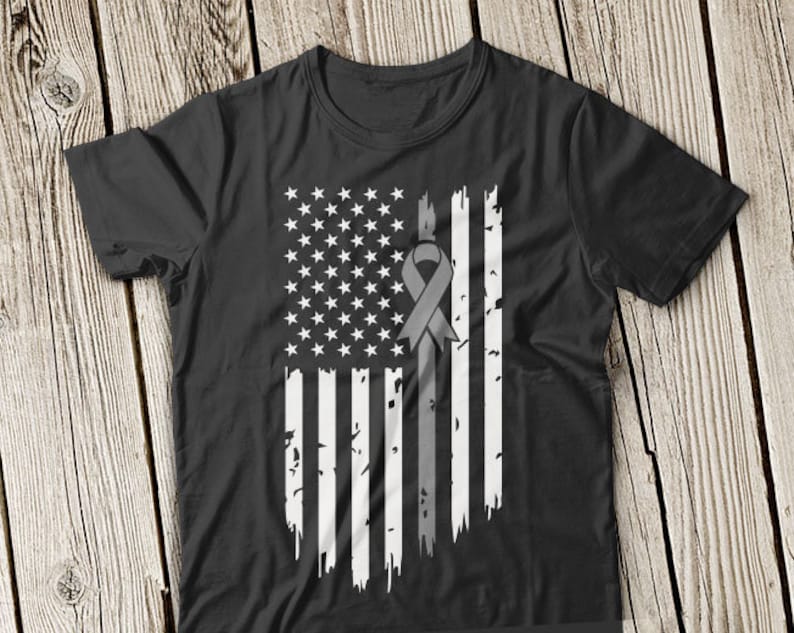 May include: Black t-shirt featuring a distressed American flag design with a gray ribbon. The flag has white stars and stripes, with the ribbon placed vertically through the center. The design has a vintage, worn look.