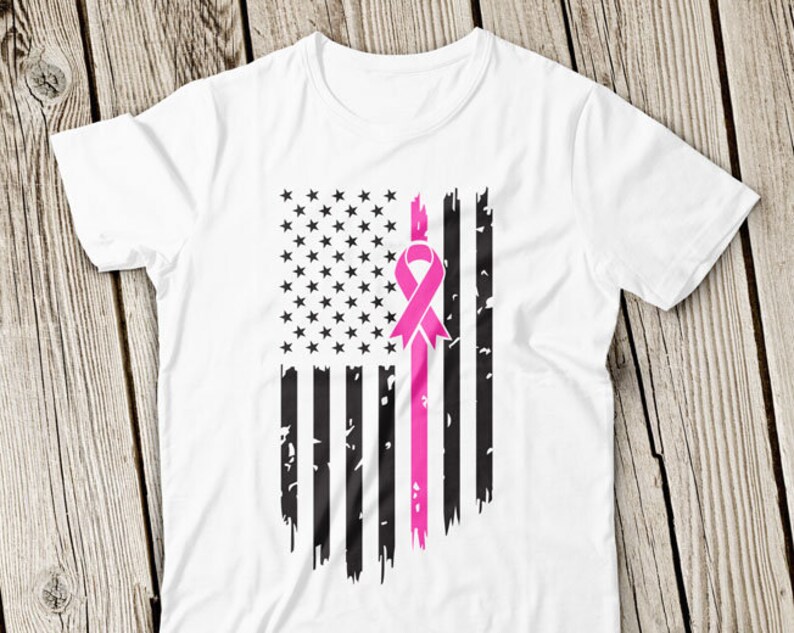 Op de afbeelding: Een wit T-shirt met een verweerd Amerikaans vlagontwerp met een roze lint in het midden. De vlag is zwart-wit met een roze lint in het midden.