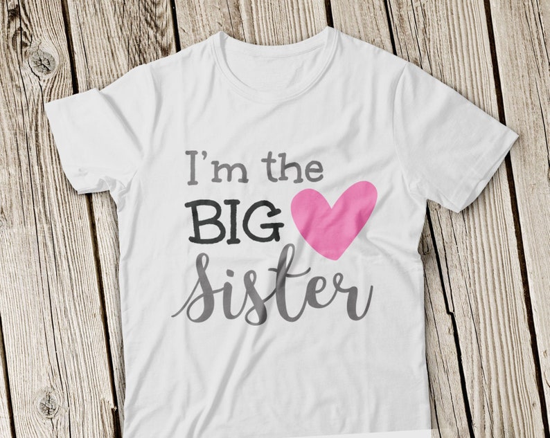 May include: White t-shirt with the text "I'm the BIG sister" in black and gray lettering. A pink heart is next to the word "BIG".