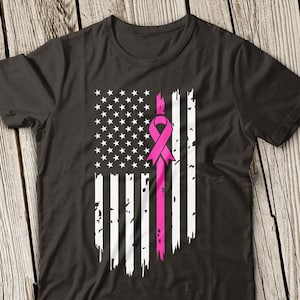 Op de afbeelding: Een zwart T-shirt met een verweerd Amerikaans vlagontwerp met een roze lint in het midden. Het lint is een symbool voor bewustwording van borstkanker.