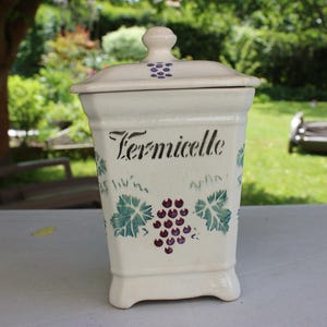 Peut inclure: Pot en céramique blanche avec un couvercle, décoré de feuilles vertes et de raisins violets. Le pot est étiqueté "Vermicelle".