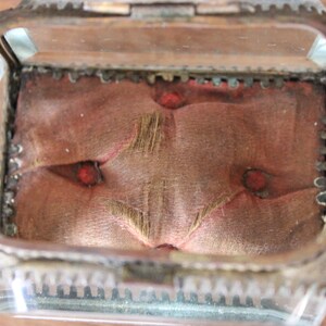 May include: A small, glass-topped jewelry box with a red velvet interior. The box has a decorative, ornate metal frame.