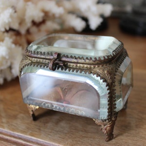 May include: A small, clear glass box with a gold metal trim and feet. The box has a hinged lid with a metal clasp.