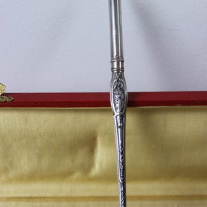 Op de afbeelding: Een set zilveren gereedschap in een doos met een rode fluwelen voering. De gereedschappen omvatten een briefopener, een papiermes en een schaar.