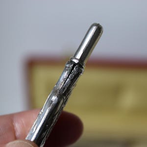 Op de afbeelding: Een gedetailleerde, decoratieve pen in zilverkleur met een puntige punt.