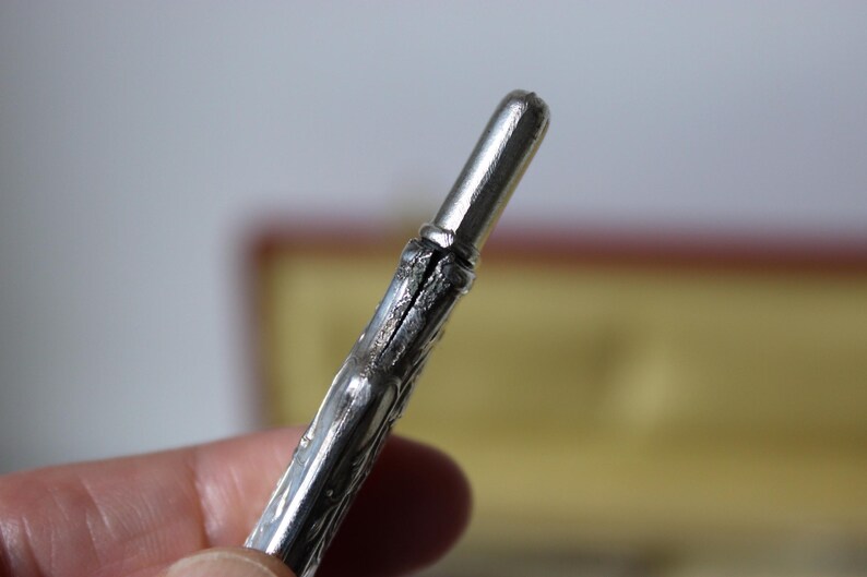 Op de afbeelding: Een gedetailleerde, decoratieve pen in zilverkleur met een puntige punt.