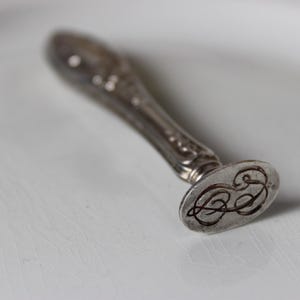 Op de afbeelding: Een zilveren zegel met een decoratief handvat en een ronde zegel met een monogram.