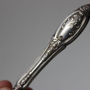 Op de afbeelding: Close-up van een zilveren, sierlijke, decoratieve handgreep van een vintage bestek.