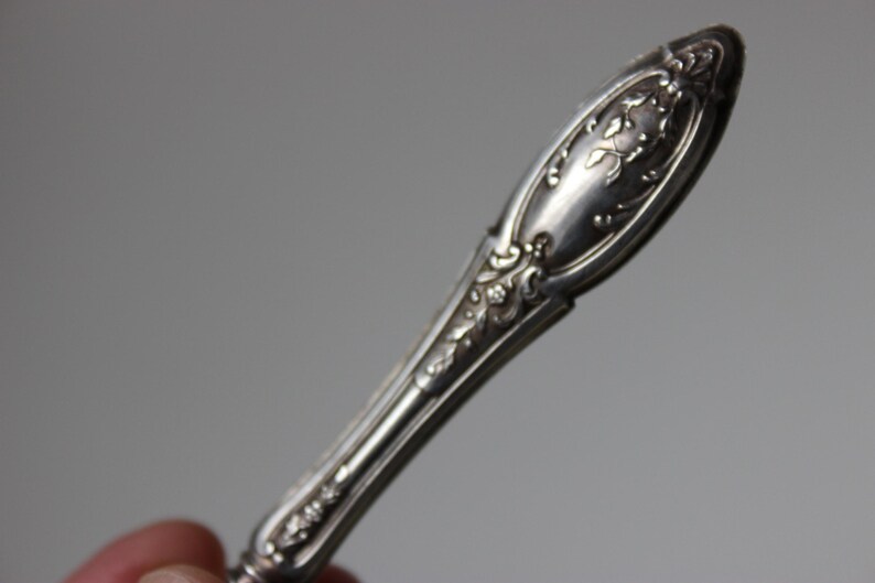 Op de afbeelding: Close-up van een zilveren, sierlijke, decoratieve handgreep van een vintage bestek.