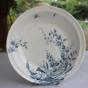 Peut inclure: Un bol rond en céramique à base crème orné d'un motif floral bleu foncé. Le design représente des tiges, des feuilles et des fleurs délicates s'étendant du bord inférieur vers le centre et les côtés de la surface intérieure du bol.