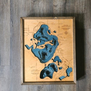 May include: A wooden map of Stone Lake in LaPorte County, Indiana. The map is framed in a dark wood frame and shows the lake's depth contours in blue. The text on the map reads "Stone Lake, LaPorte County, IN.  Deepest Point: 41 feet. Area: 140 acres."