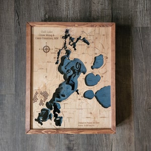 Puede incluir: Un mapa de madera enmarcado del lago Gull en los condados de Crow Wing y Cass, Minnesota. El lago está representado en azul y el área circundante en marrón. El mapa incluye el texto "Deepest Point: 80 feet" y "Area: 9,418 acres".