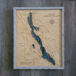 May include: A wooden map of Long Lake in Cumberland County, Maine. The map is framed in a light gray frame and shows the lake's shape and depth. The text "Deepest Point: 59 feet" and "Area: 4,867 acres" is included on the map.