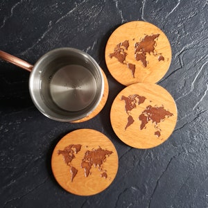 May include: Four wooden coasters with a world map design. The coasters are round and have a light brown color. A silver mug with a copper handle is sitting on top of the coasters.