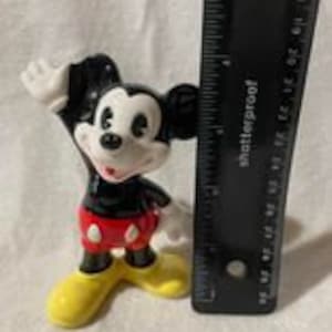May include: A black and white ceramic figurine of Mickey Mouse with red shorts and yellow shoes. Mickey is waving with his right hand.