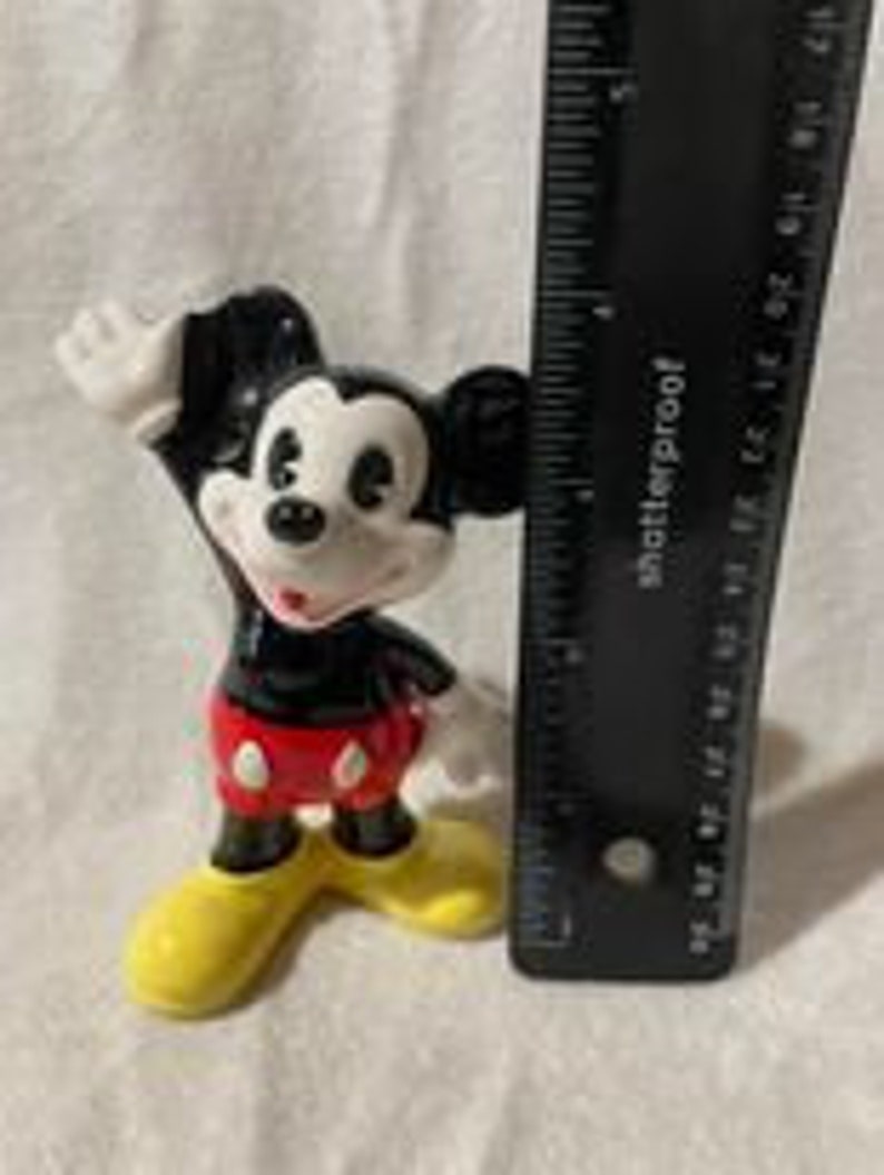 May include: A black and white ceramic figurine of Mickey Mouse with red shorts and yellow shoes. Mickey is waving with his right hand.