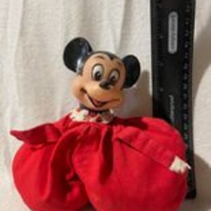 May include: A vintage Mickey Mouse plush toy wearing a red dress with white polka dots. The toy is made of soft fabric and has a smiling face.