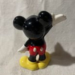 May include: A black and red ceramic figurine of Mickey Mouse with yellow shoes. Mickey is standing with his right arm raised and his left arm at his side.