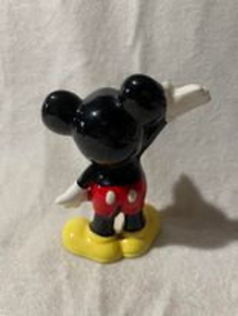 May include: A black and red ceramic figurine of Mickey Mouse with yellow shoes. Mickey is standing with his right arm raised and his left arm at his side.