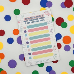 Op de afbeelding: Een roze en blauwe checklist met de tekst "Silly little tasks I must complete before I can read my book". De checklist heeft 10 lege regels om taken op te schrijven.