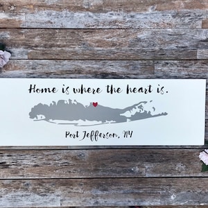 Könnte beinhalten: Ein weißes Holzschild mit dem Text "Home is where the heart is." und einer grauen Umrandung von Long Island, New York mit einem roten Herzen, das den Ort Port Jefferson, NY markiert.