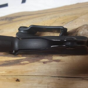 May include: A black gun holster with a built-in trigger guard. The holster is made of a durable plastic material and has a smooth, matte finish.