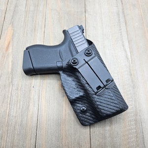 May include: A black handgun in a black carbon fiber holster with a black metal clip.