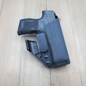 May include: A black handgun holster with a clip and a SIG SAUER pistol inside.