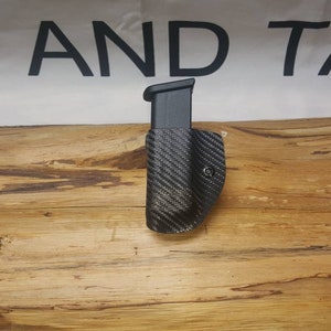 May include: A black carbon fiber magazine holster for a handgun. The holster is designed to be worn on a belt.