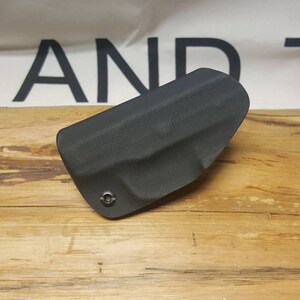 May include: A black leather holster for a firearm. The holster has a single screw on the front.