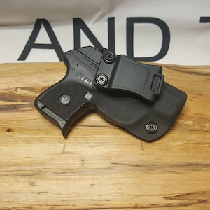 May include: A black handgun with a black holster and a clip. The holster has a black clip that attaches to a belt.