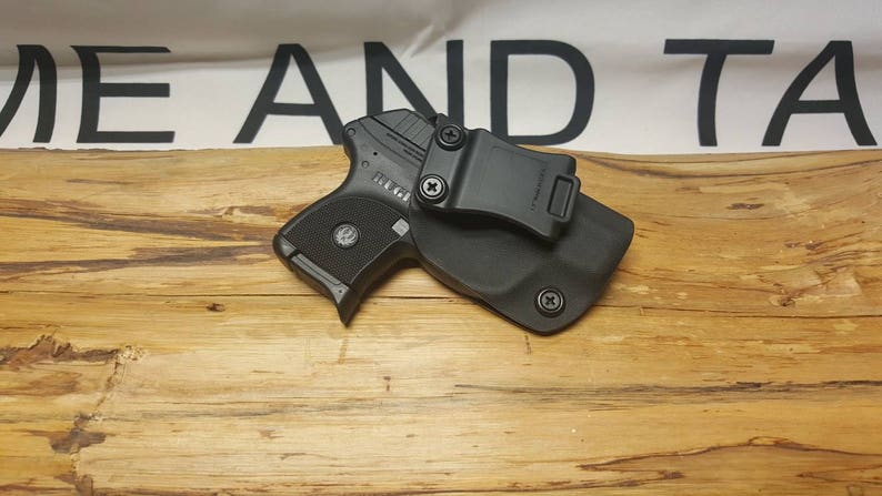 May include: A black handgun with a black holster and a clip. The holster has a black clip that attaches to a belt.